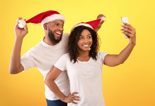 Natale e Capodanno insieme. Gioioso afro-americano sposi divertirsi con Babbo Natale cappelli e prendere selfie - Foto, immagini