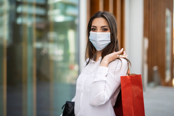 Young woman shopping in a city while wearing a mask - Valokuva, kuva