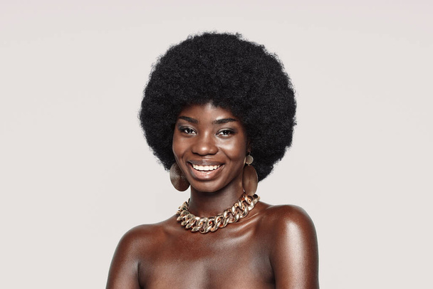 Portrait of beautiful young African woman in golden jewelry looking at camera and smiling - Fotó, kép