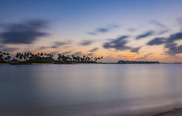 Palmy na tropikalnym wybrzeżu o zachodzie słońca. Skrzyżowanie Malediwów, hotel hard rock, czerwiec 2021. Obraz długiej ekspozycji - Zdjęcie, obraz