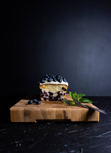ブルーベリーケーキクリームチーズガナッシュダークな背景の木の板に - 写真・画像