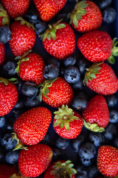 Background of assorted fresh berries of red juicy strawberries and blue blueberries close-up. View from above - Photo, Image