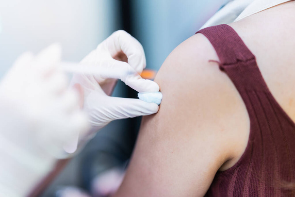 Bir hemşire COVID-19 'a karşı aşı yapmadan önce, bir kadının üst kolunda alkole batırılmış pamuk bezi kullanıyor.. - Fotoğraf, Görsel