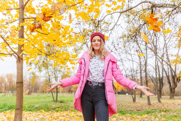 Ευτυχισμένη νεαρή γυναίκα παίζει κάτω από την πτώση κίτρινα φύλλα σε όμορφο πάρκο φθινόπωρο στη φύση βόλτες σε εξωτερικούς χώρους. Η έφηβη ξερνάει φύλλα πορτοκαλιού. - Φωτογραφία, εικόνα
