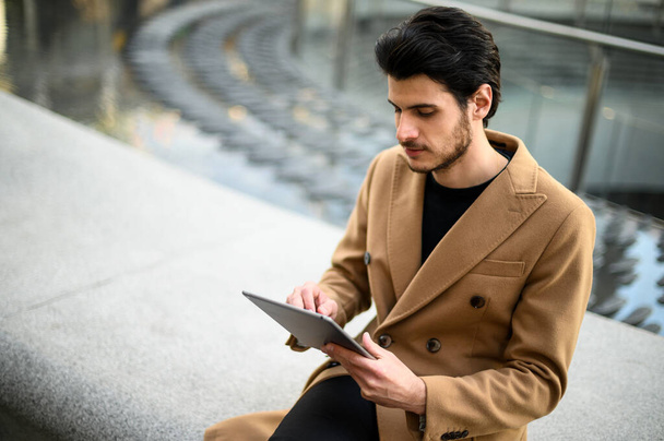 Handsome young man using a digital tablet on a bench outdoor - Foto, Bild