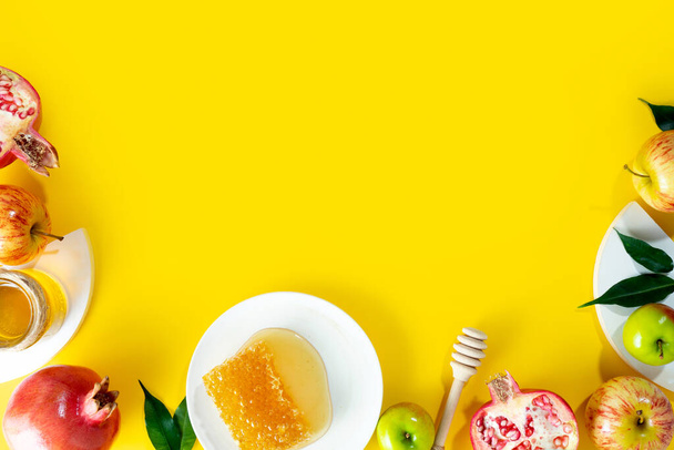 Honey, apple and pomegranate on a yellow background. Concept Jewish New Year Happy holiday Rosh Hashanah. Creative layout of traditional symbols. View from above. Flat lay. Copy space. Shana Tova. - Photo, Image