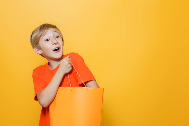 il ragazzo ha messo la mano in un sacchetto di carta arancione ed è felice - Foto, immagini