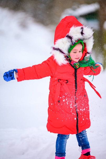 A happy girl in a red jacket and Ukrainian national kerchief walks in a snowy yard. new - Zdjęcie, obraz