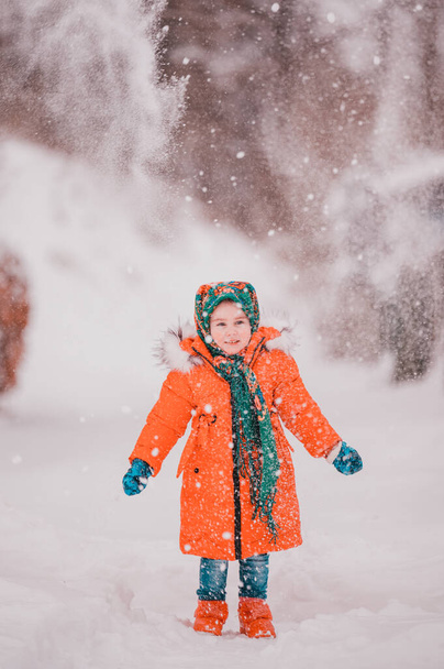 Kırmızı ceketli mutlu bir kız ve Ukrayna ulusal eşarbı karlı bir bahçede yürüyor. yeni - Fotoğraf, Görsel