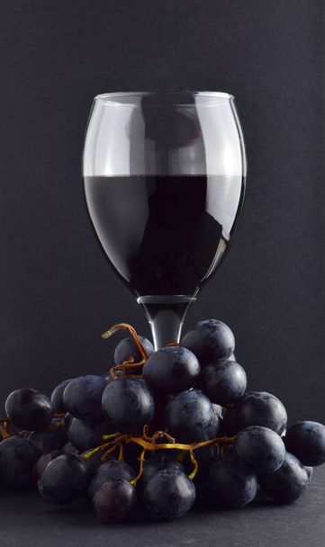 Ποτήρι κρασιού και μαύρα σταφύλια. Σκούρο φόντο και αντίγραφο χώρου. - Φωτογραφία, εικόνα