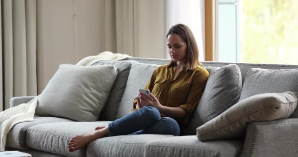 Mujer atractiva sentarse en el sofá en la sala de estar con teléfono inteligente - Metraje, vídeo