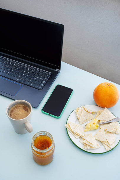 Telecommuting reggelivel az asztalon, laptop és okostelefon, grapefruit és keserű narancs latte - Fotó, kép