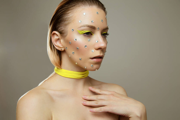 Studio portrait of beautiful girl with creative bright yellow makeup with rhinestones - Foto, imagen