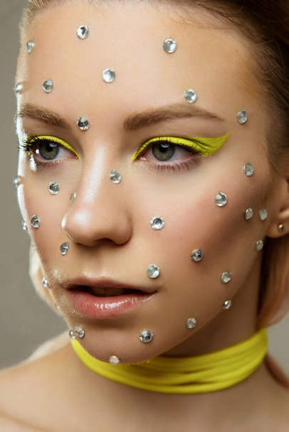 Studio portret van mooi meisje met creatieve heldere gele make-up met strass - Foto, afbeelding