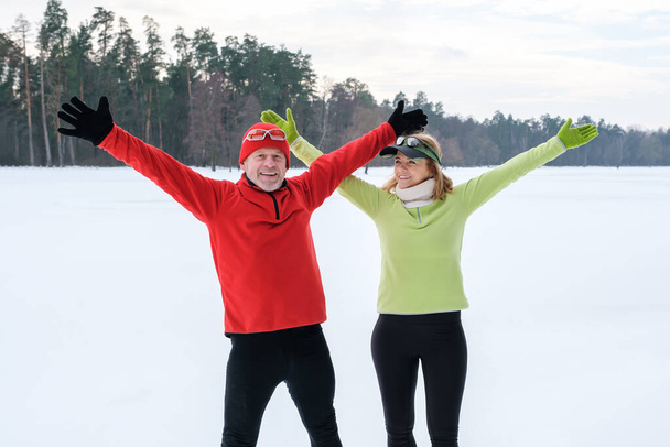 Smiling mature couple with outstretched arms in park in winter - Photo, Image