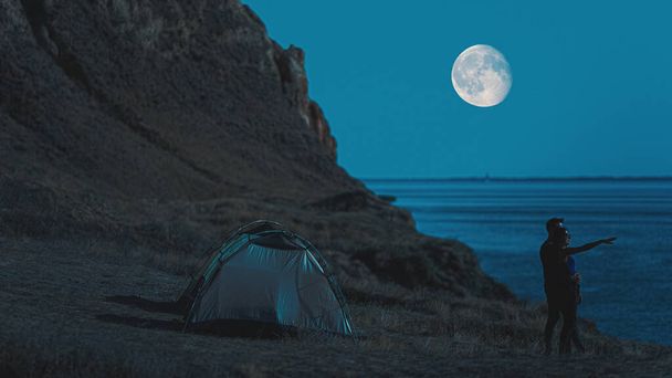 夜の海の景色を背景にキャンプテントの近くに立っているカップル - 写真・画像