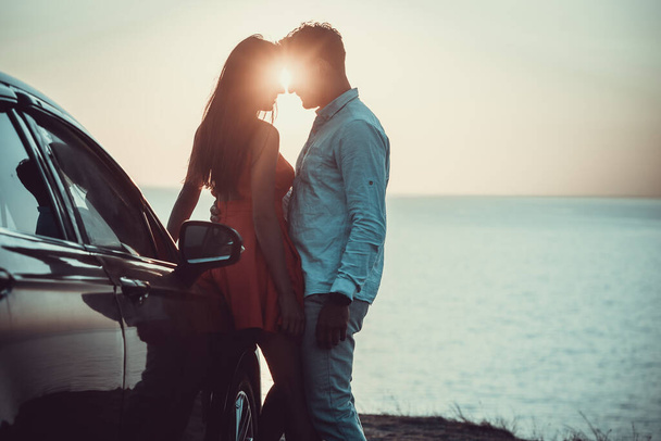 Το όμορφο ζευγάρι στέκεται κοντά στο αυτοκίνητο στην ακτή της θάλασσας - Φωτογραφία, εικόνα