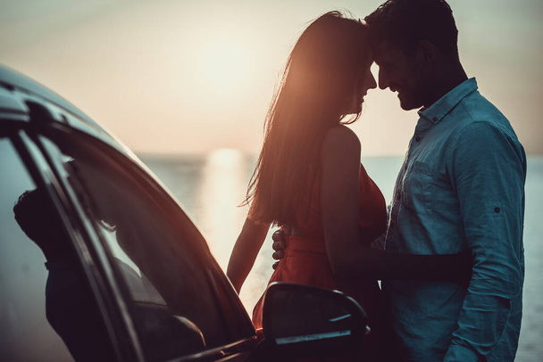 Ο άντρας και η γυναίκα στέκονται κοντά στο αυτοκίνητο στην ακτή. - Φωτογραφία, εικόνα