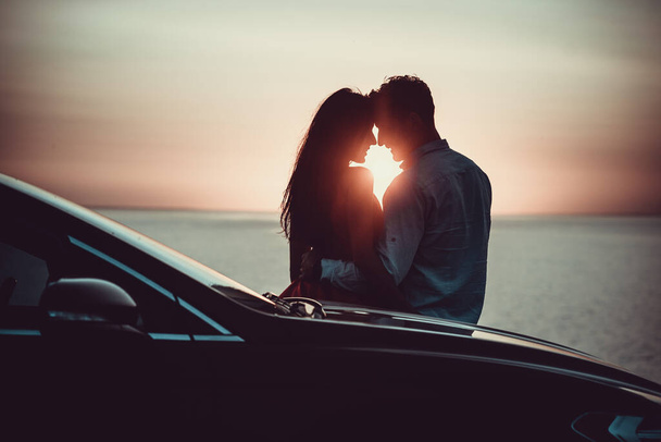 La pareja romántica de pie cerca del coche en el hermoso fondo de la puesta del sol - Foto, imagen