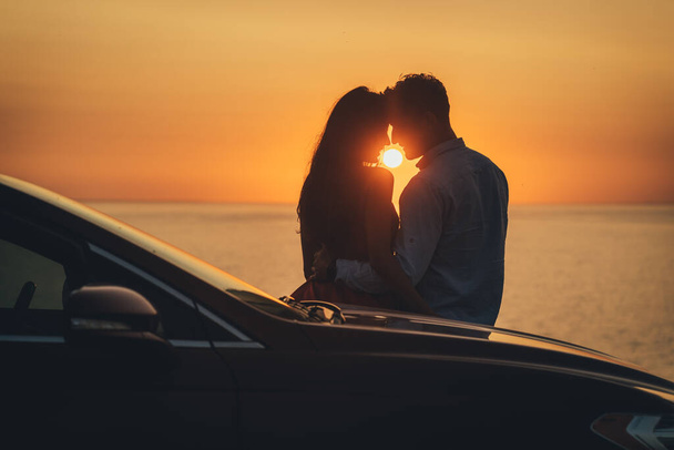 Romanttinen pari seisoo lähellä autoa kauniilla auringonlaskun taustalla - Valokuva, kuva