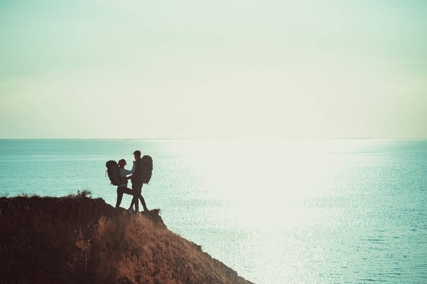 The two travelers with backpacks standing on the mountain top near the sea - Foto, Imagen