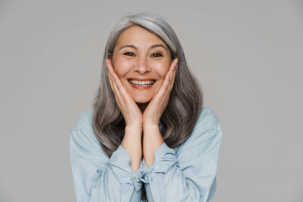 Mature white-haired woman smiling and looking at camera isolated over gray wall - Foto, afbeelding