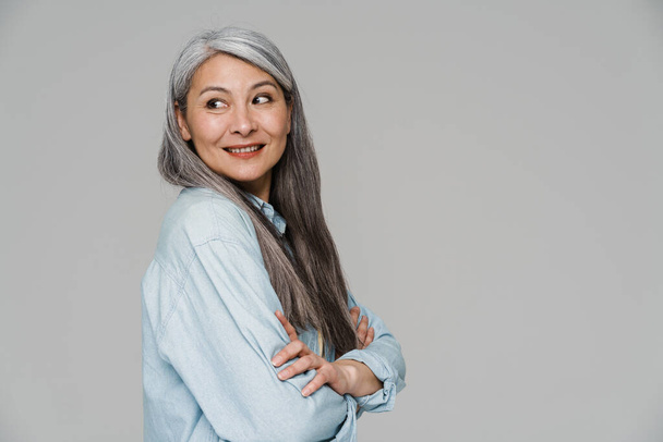 Mature white-haired woman smiling and looking aside isolated over gray wall - Foto, afbeelding