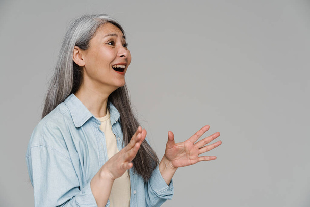 Surprised white-haired woman gesturing and looking aside isolated over gray wall - Foto, Imagem