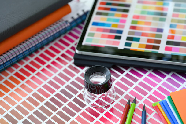 Μικρός μεγεθυντικός φακός πάνω από την παλέτα χρωμάτων και τα δείγματα με διαφορετικές αποχρώσεις closeup - Φωτογραφία, εικόνα