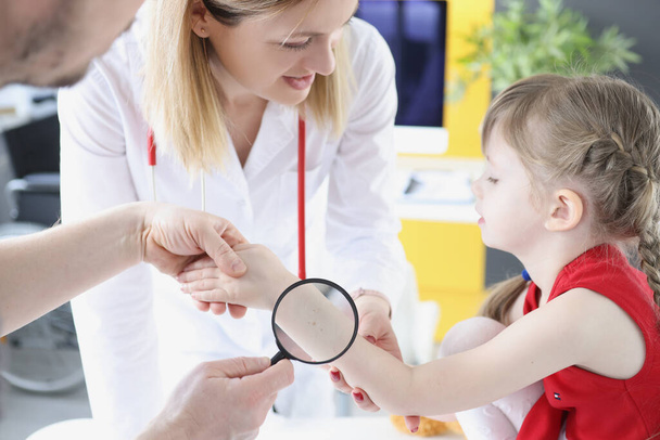 Врач, осматривающий детскую кожу под рукой с лупой в клинике - Фото, изображение