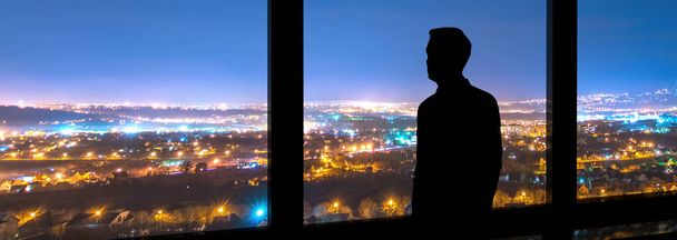 A férfi az ablak mellett áll a városkép hátterében. - Fotó, kép