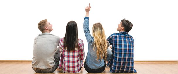 The four friends sit on the floor and gesture on a white wall background - Photo, image