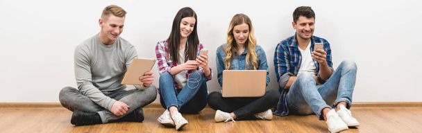 The four happy people sit on the floor with gadgets on the white background - Photo, Image