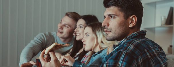 Τα τέσσερα άτομα με πίτσα βλέπουν μια ταινία στον καναπέ. - Φωτογραφία, εικόνα