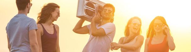 The happy people stand with a boom box on the bright sun background - Photo, Image