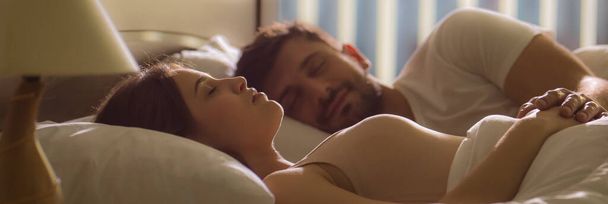 Молода жінка спить біля чоловіка в ліжку
 - Фото, зображення
