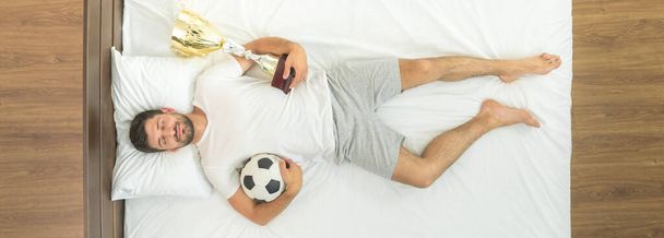 O homem com um copo e uma bola a dormir na cama. vista de cima - Foto, Imagem