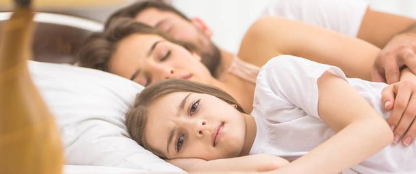 Το κορίτσι ξάπλωσε δίπλα στους κοιμισμένους γονείς στο κρεβάτι. - Φωτογραφία, εικόνα