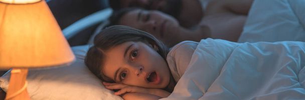 Przestraszona dziewczyna leżała obok śpiących rodziców w łóżku. Czas nocny - Zdjęcie, obraz