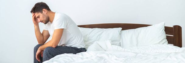 Несчастный человек сидит на кровати на белом фоне - Фото, изображение