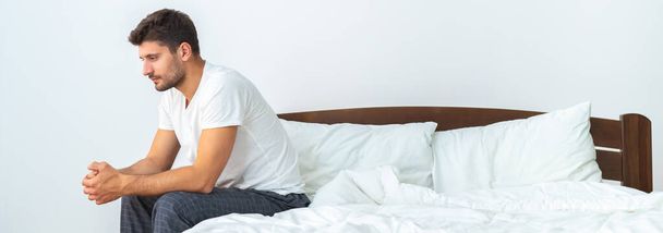 Masentunut mies istuu sängyllä valkoisella taustalla - Valokuva, kuva
