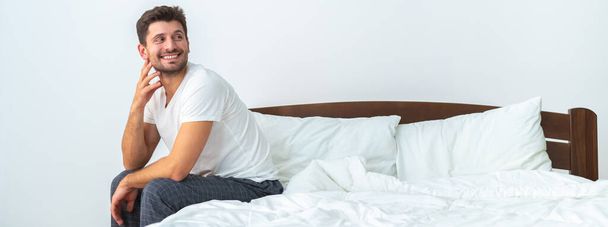 Щасливий чоловік сидить на ліжку на білому тлі
 - Фото, зображення