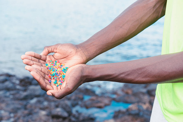 Hands full of microplastics on the beach. Different plastic colored ... Plastic pollution concept. - 写真・画像