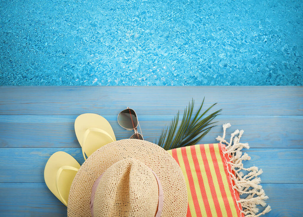 Beach towel, flip flops, sunglasses and straw hat on blue wooden surface near swimming pool, flat lay - Фото, изображение
