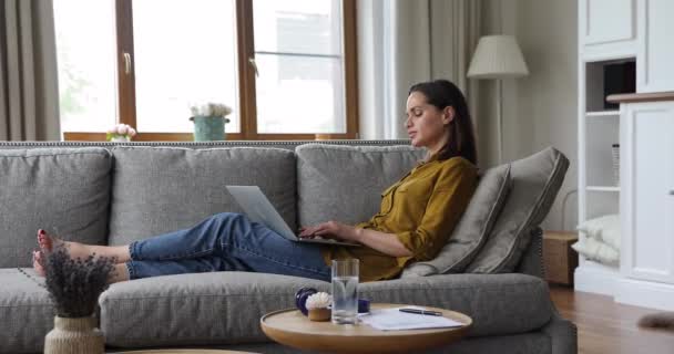 Young serious woman sit on sofa working on laptop - Felvétel, videó