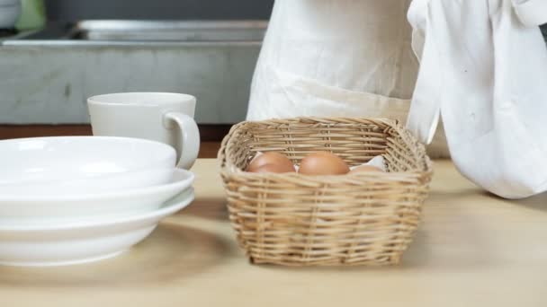 Κοντινό πλάνο, θηλυκό σεφ φέρνει φρέσκα βιολογικά αυγά από την τσάντα και τα στοιβάζει στο καλάθι στο ξύλινο τραπέζι στην κουζίνα του σπιτιού πριν μαγειρέψουν ως πρωινό γεύμα, υγιεινές πρωτεϊνούχες τροφές, αλλά υψηλές θερμίδες.  - Πλάνα, βίντεο