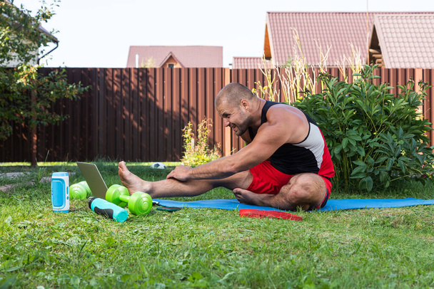 Close-up van een jonge man in een sportuniform proberen mediteert in moeilijke positie, stretching op de vloer in de achtertuin in de zomer zeggen - Foto, afbeelding