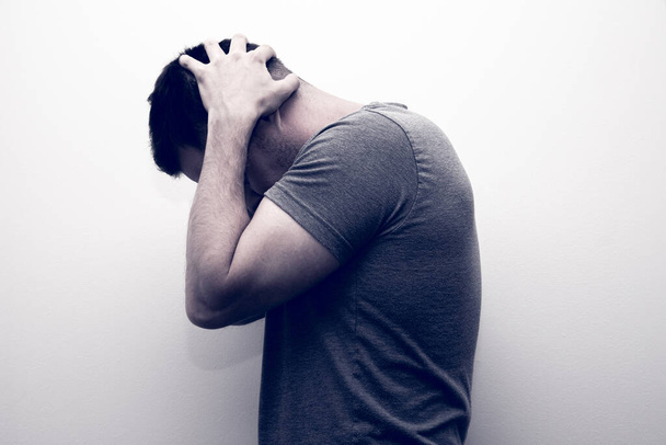 A depressed miserable adult man holding his head with his hands against the wall - Fotoğraf, Görsel