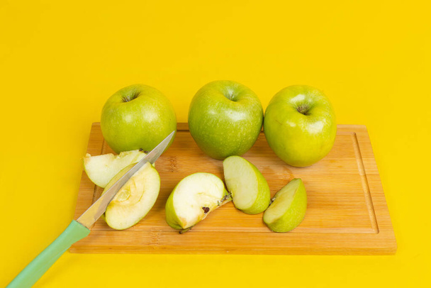 A closeup of ripe green apples on a cutting board with a knife on it isolated on a yellow background - Foto, afbeelding