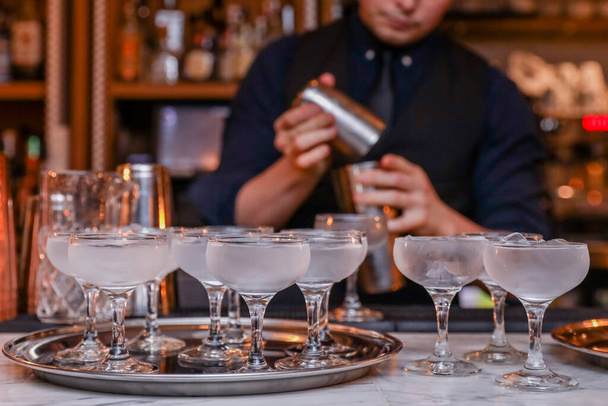 Barkeeper macht Cocktail im Shaker in der Nähe von Metalltablett voller Gläser - Foto, Bild